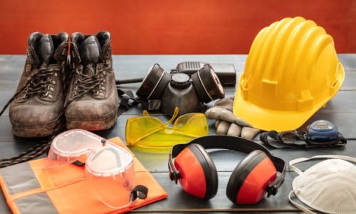Work safety protection equipment. Industrial protective gear on wooden table, red color background. Construction site health and safety concept